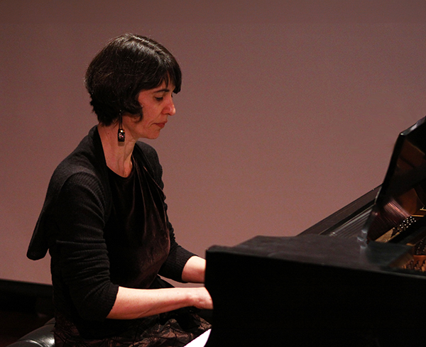A woman with short dark hair plays the piano
