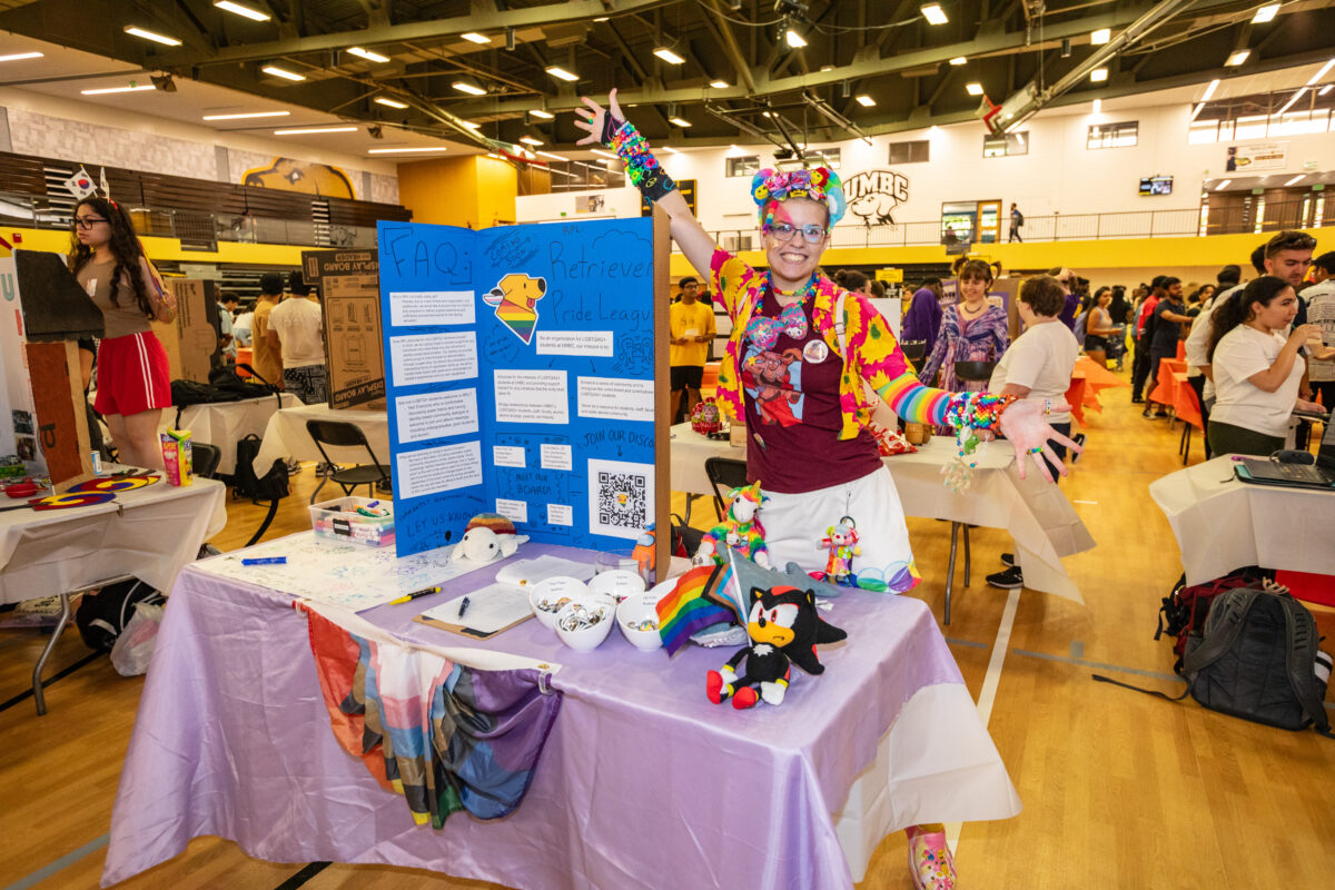 A student wearing colorful clothes poses next to a display of information about their club.