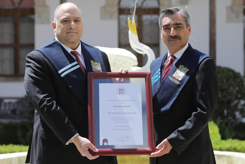 Two mean wearing formal attire hold a framed certificate.