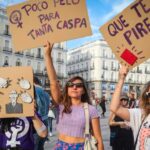 A group of women stand in a plaza holding cardboard signs protesting against sexism in Spain.