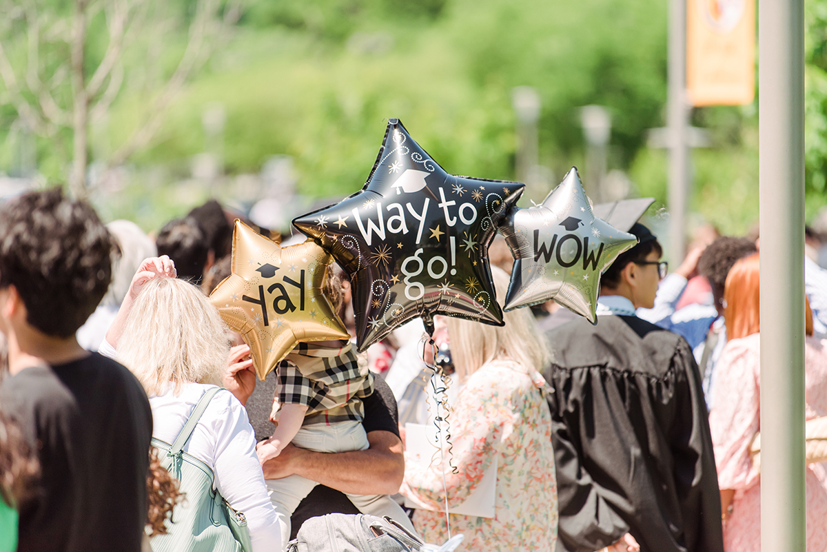 Star-shaped balloons that read, Yay, Way to go, and Wow, held by family members of graduating UMBC students.