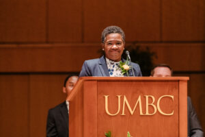 a woman stands behind a lectern that says UMBC