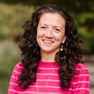 Outdoor professional headshot of Angela Paik, wearing a pink striped sweater and necklace
