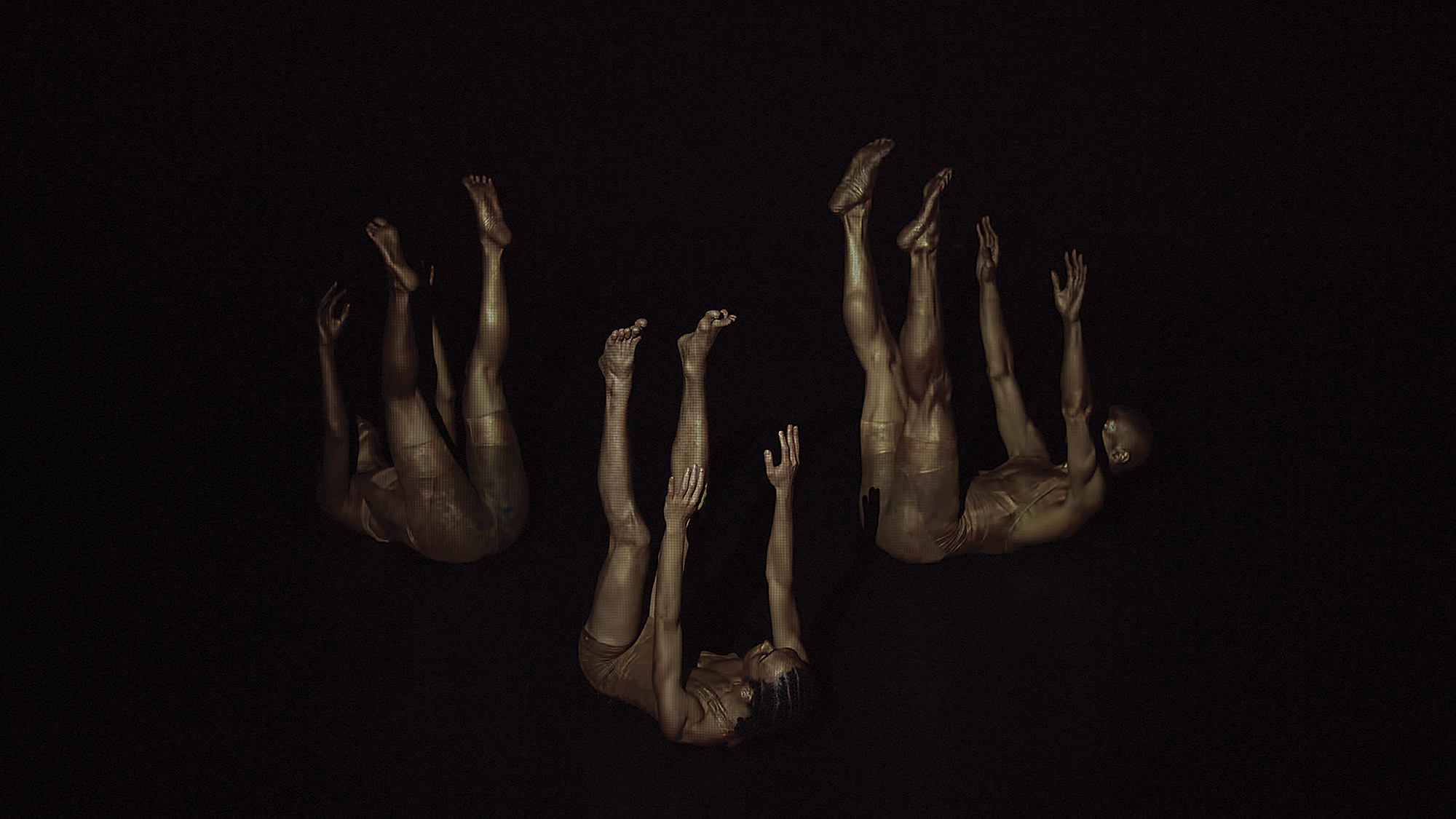 In a dimly lit scene, three dancers are on their back with their limbs extended up