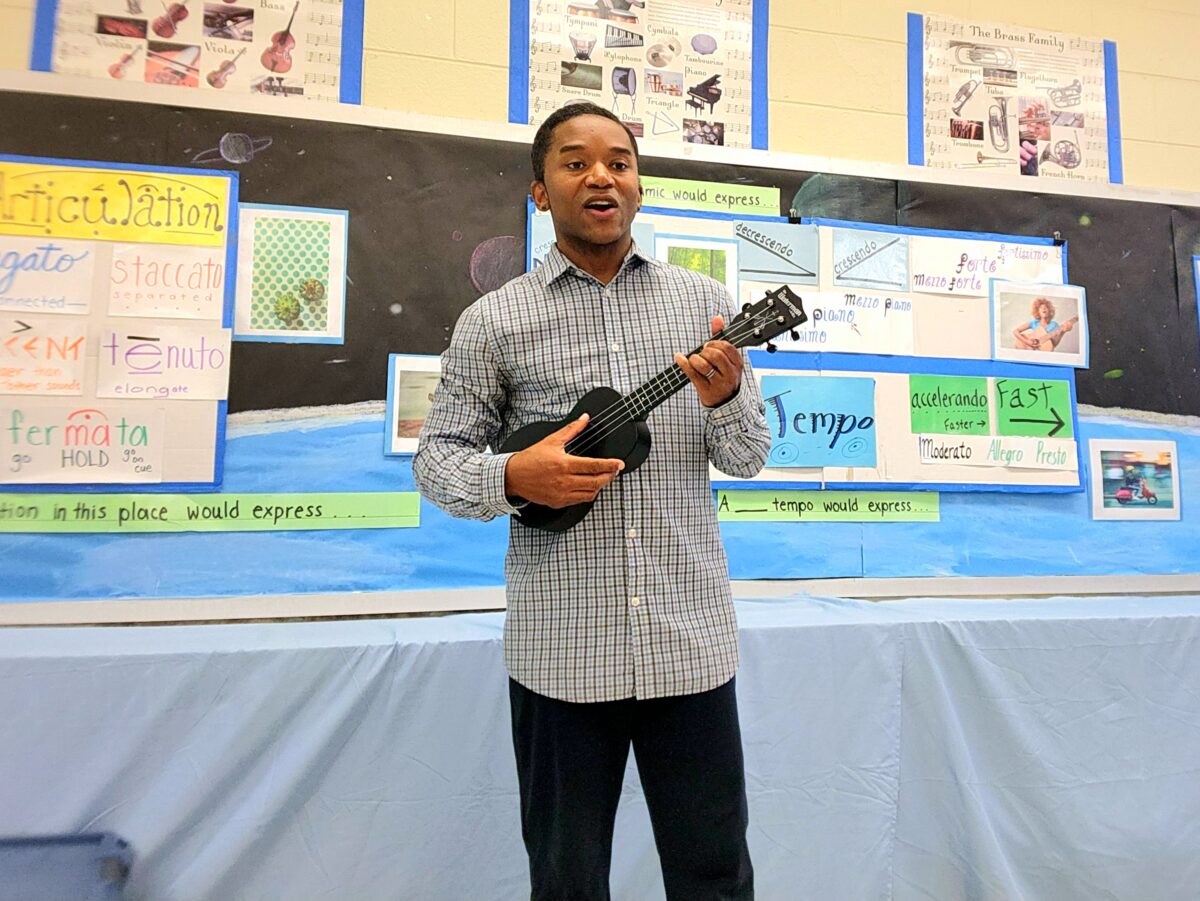 A teacher plays a ukulele in front of a classroom