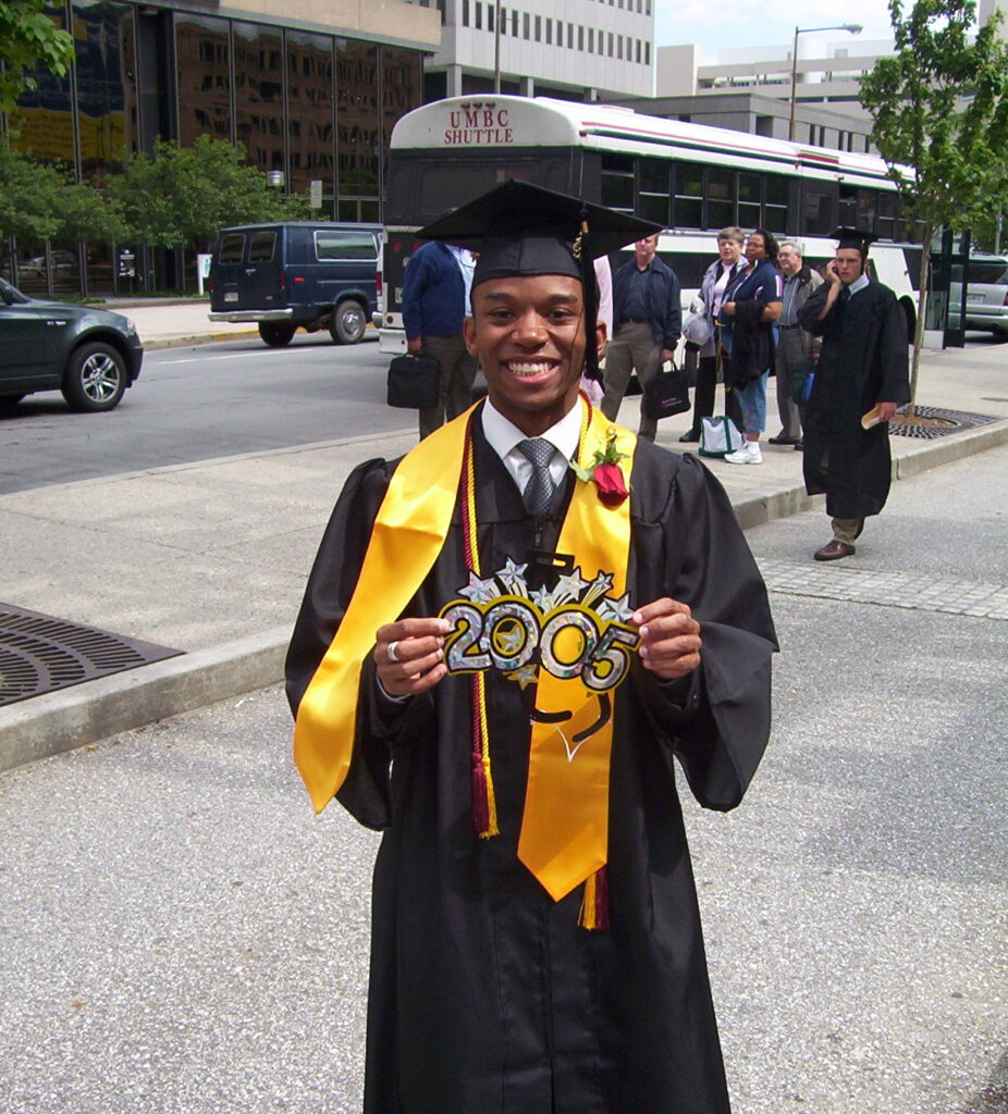 a student in a grad cap and gown stands with a 2005 sign