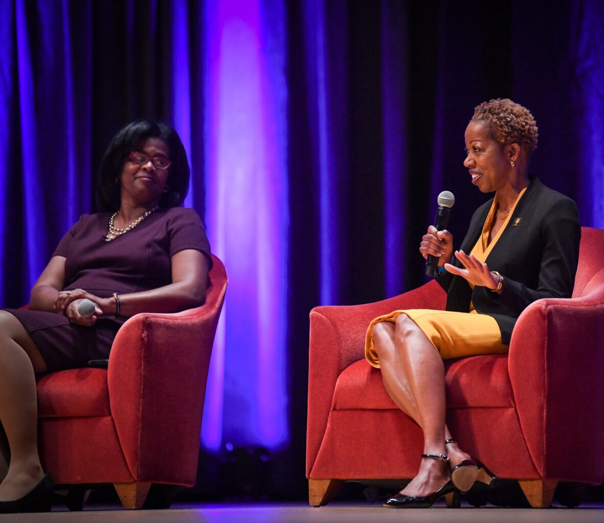 Two women sitting on stage while holding microphones during the Baltimore Banner's Impact Maryland 2023 event.