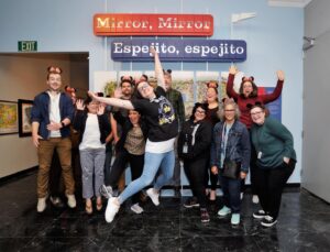a group of people in Minnie Mouse ears jumps in front of an exhibit that says Mirror, Mirror