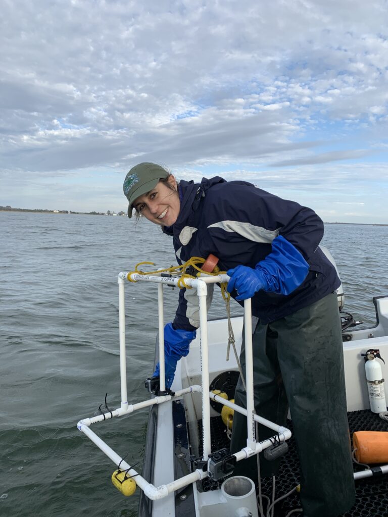 woman on boat smiling at camera holding PVC pipe structure with camera attached over the edge of the boat