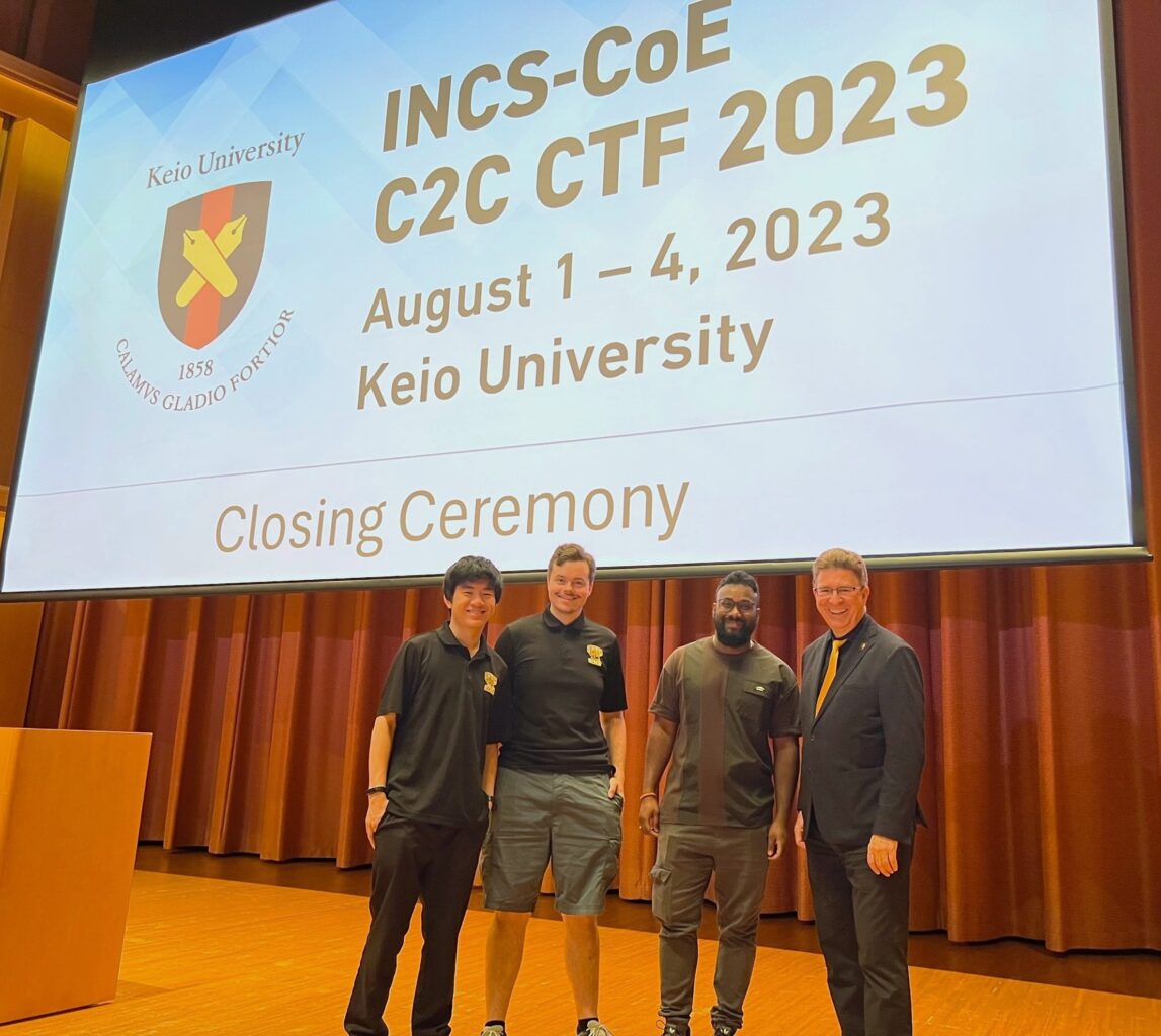 Four men standing on stage in front of a screen that says "INCS-COE C2C CTF 2023, August 1-4, 2023, Keio University, closing ceremony"