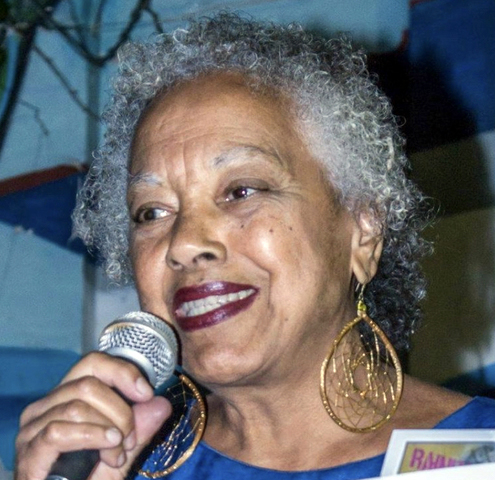 A Black woman with gray hair holds a microphone