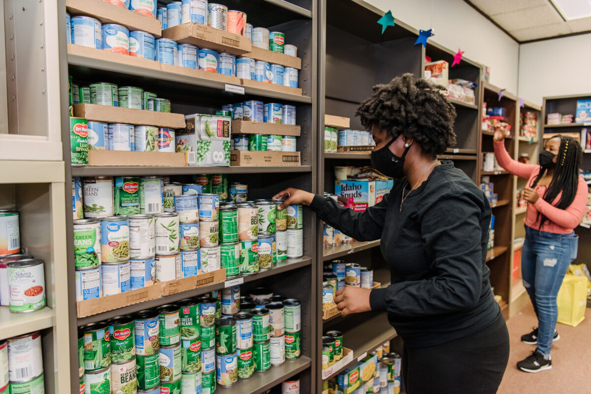Students in face masks stand stocking shelves in a pantry