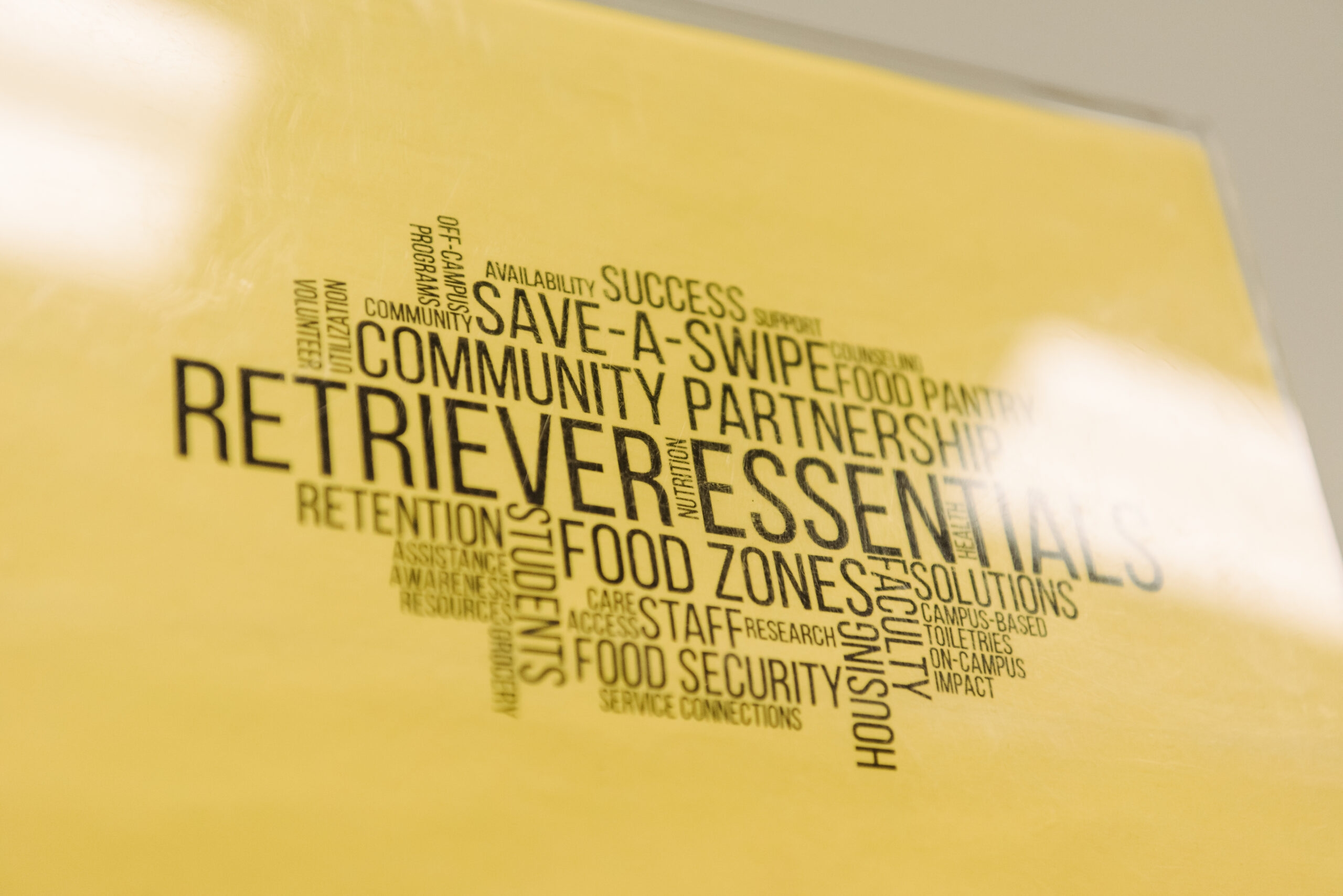 Printed text on yellow background as a word cloud, including words "Retriever Essentials. Community partnerships. Save-a-swipe"