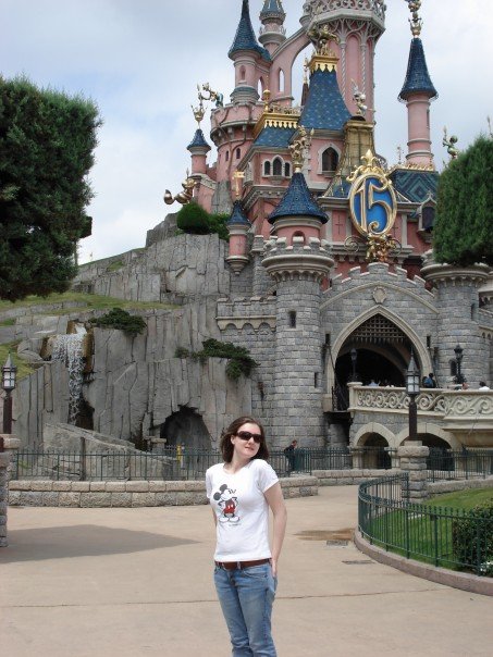 A woman in a Mickey Mouse shirt stands in front of a Disney castel