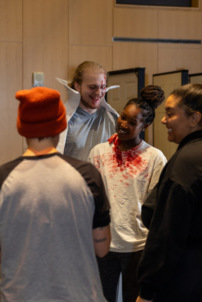 in rehearsal, dracula looks at the neck of his next victim. Two directors stand nearby.