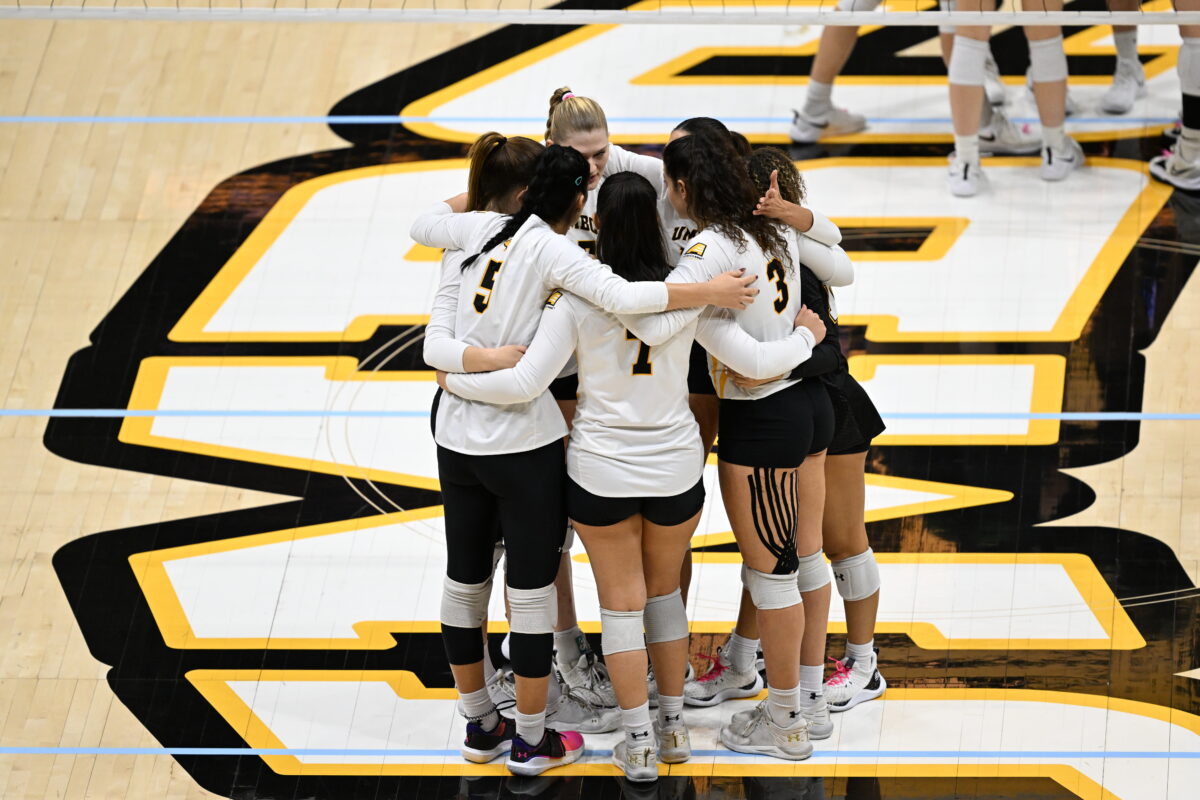 A group of volleyball players huddle up on the UMBC court