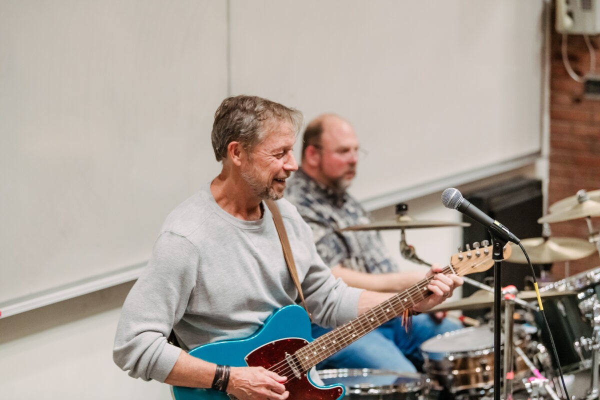 a man plays a teal guitar and another man plays the drums