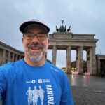 a man in running gear stands in front of the brandenburg gate in Berlin Germany