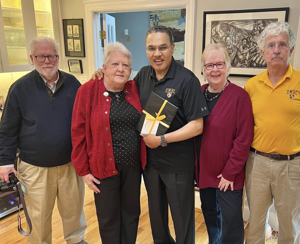 A group of alums stand with university president holding a gift
