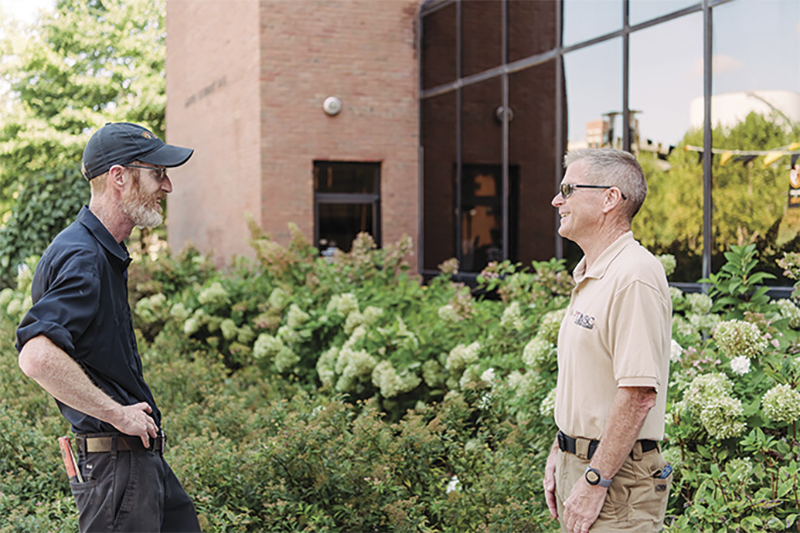 Chris Hogan, UMBC's landscape manager, speaking with another staff member outside, surrounded by greenery.