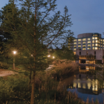 UMBC's campus at night, featuring the Albin O. Kuhn library and reflective pond, with street lamps lighting a path.