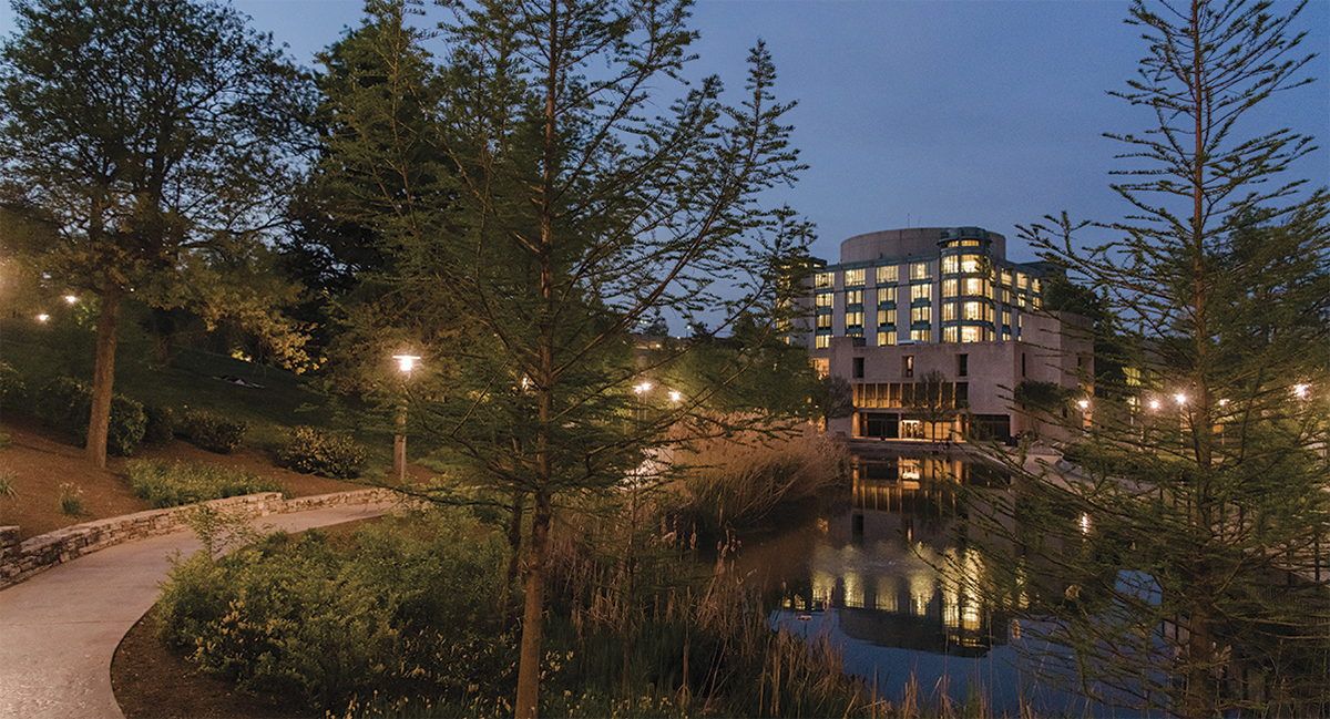 UMBC's campus at night, featuring the Albin O. Kuhn library and reflective pond, with street lamps lighting a path.