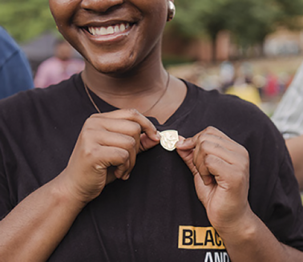 A young black woman showing off her UMBC shield pin.