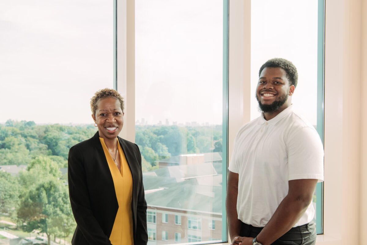 a woman and a man pose together in front of floor to ceiling windows