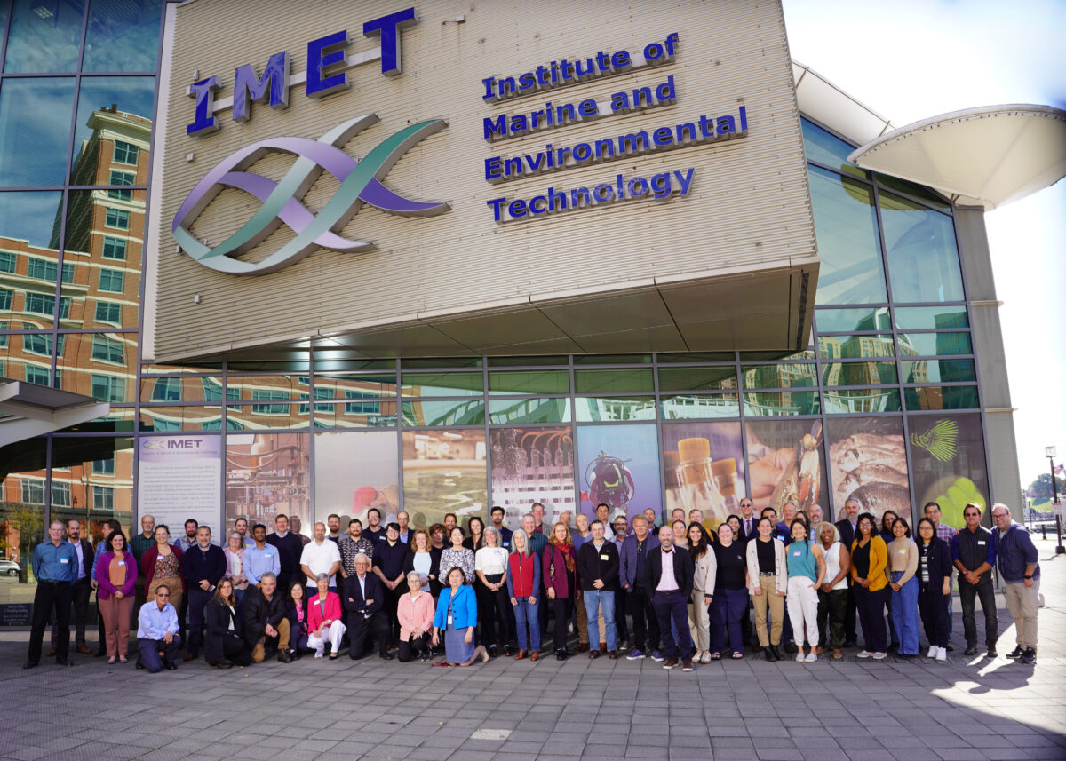 Large group photo in front of the IMET building, IMET fish logo and institute name on building above the group