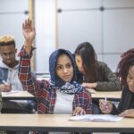 A person in a classroom wearing a hijab raises their hand. asylum-seekers