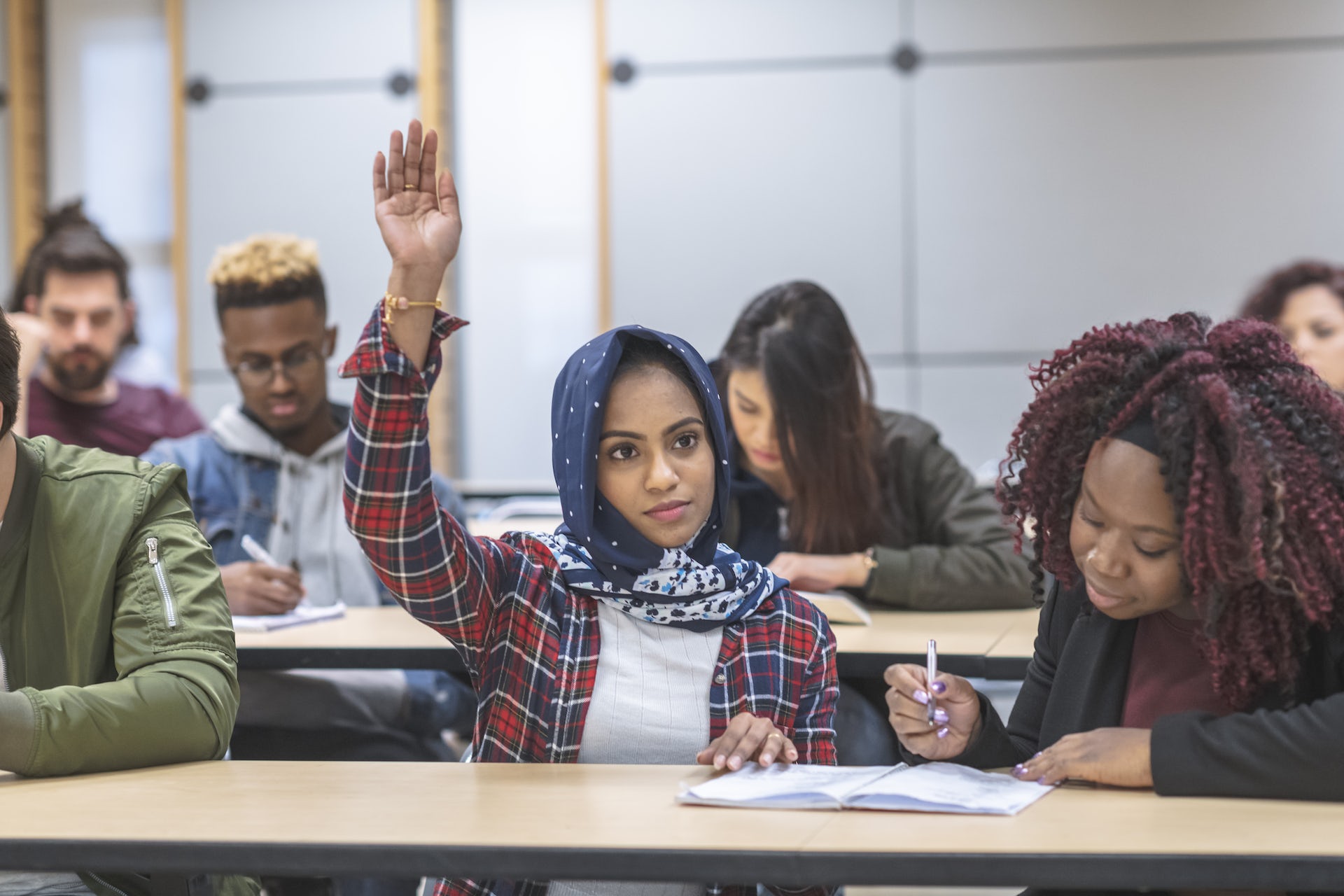 A person in a classroom wearing a hijab raises their hand. asylum-seekers