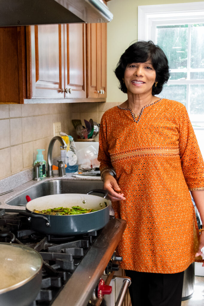 a woman stands in an orange tunic in front of a stove, following a recipe
