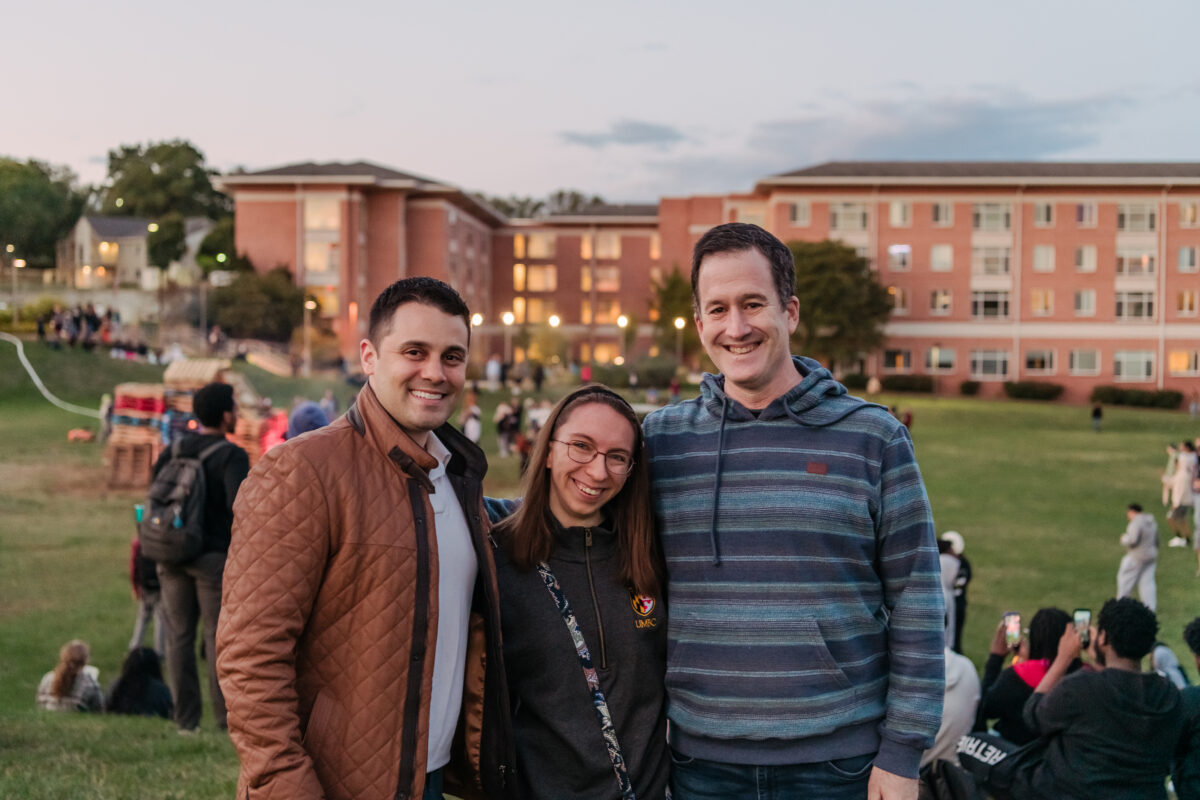 three people pose outside at dusk in front of a dorm building