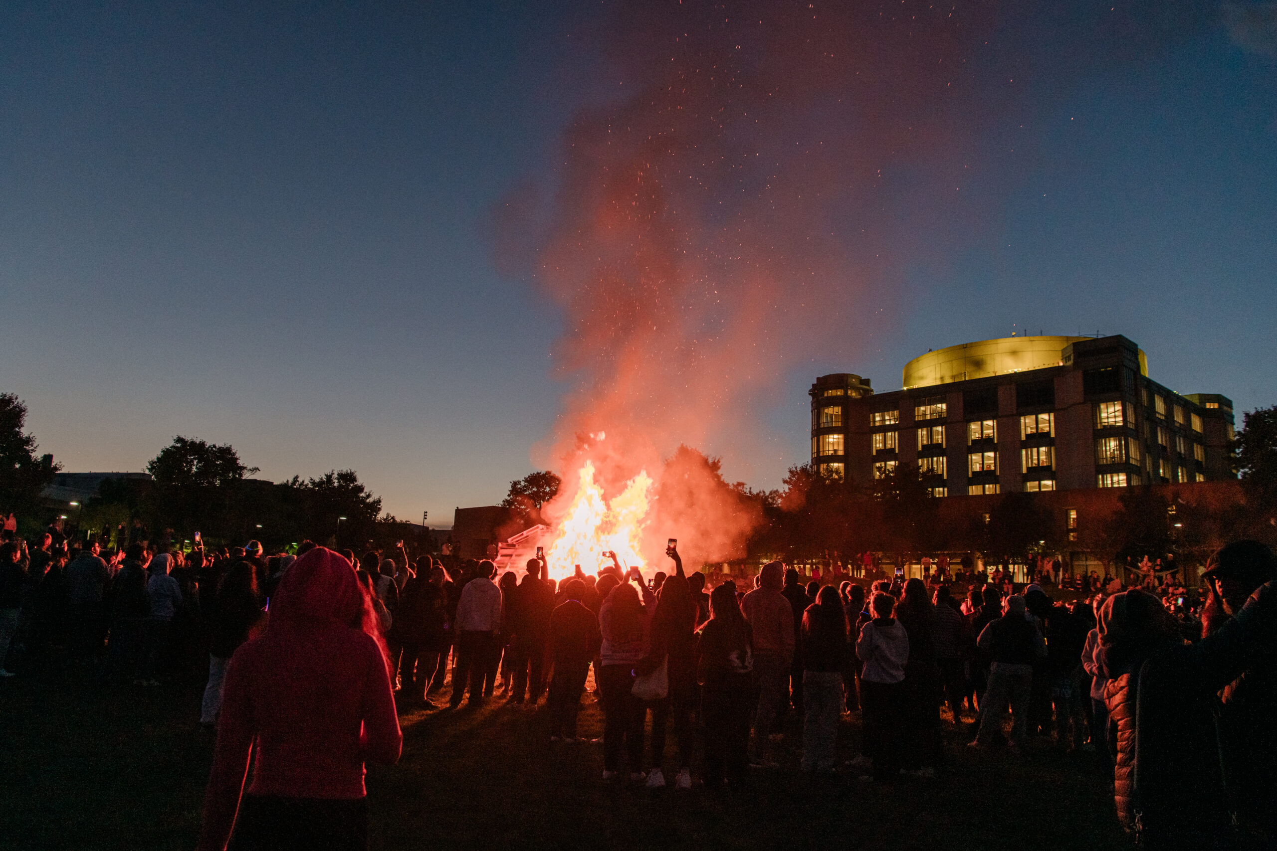 a crowd gathers at a bonfire at dusk