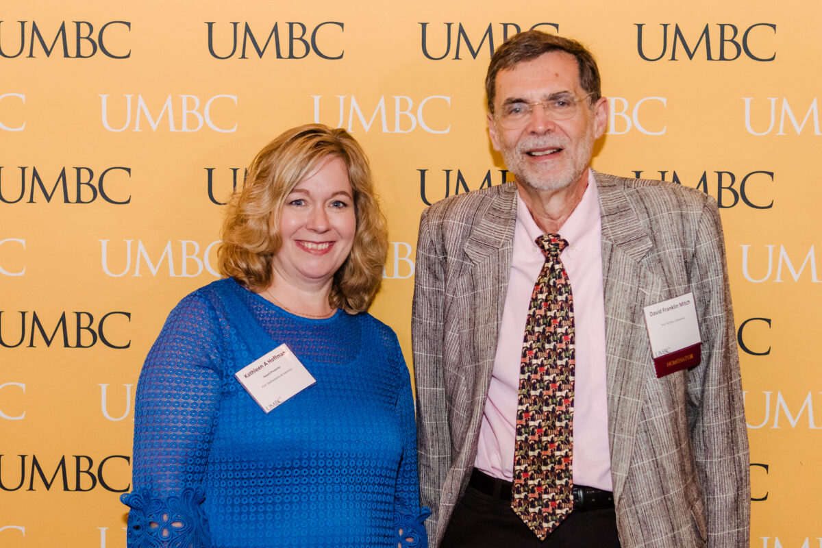 Kathleen Hoffman and David Mitch posing in front of a backdrop that says UMBC. 