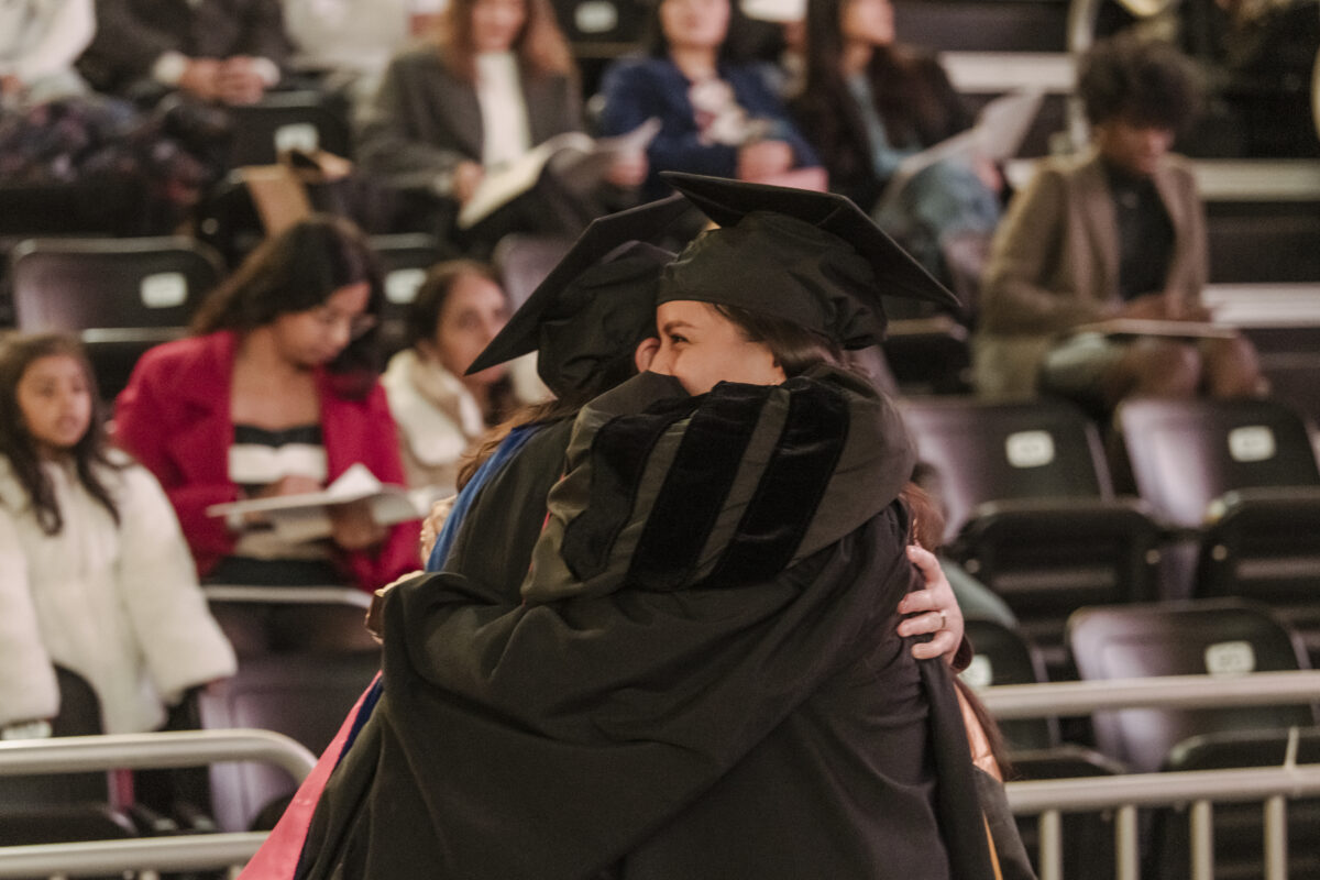 A graduate and a professor hug at a graduation