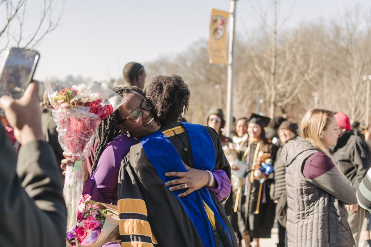An outdoor shot of a crowd, focused on someone hugging a graduate 