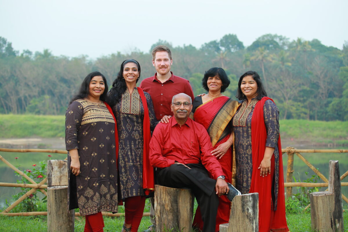 A family dressed in saris poses together outside in a wooded area