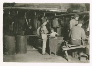 A young child works in a glass factory in a 1909 black and white historical photo by lewis hine