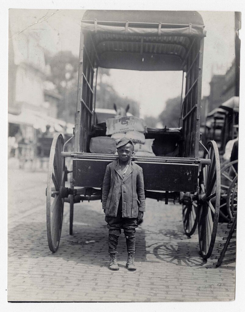a young boy stands behind a wagon in a historical black and white photo