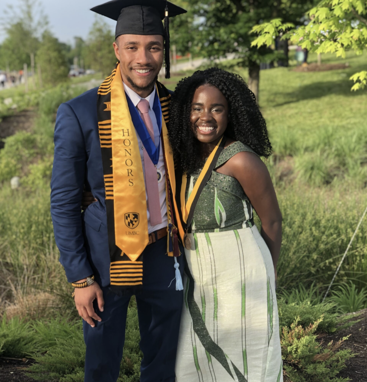 Two UMBC graduates posing and smiling for a photo on UMBC's campus.