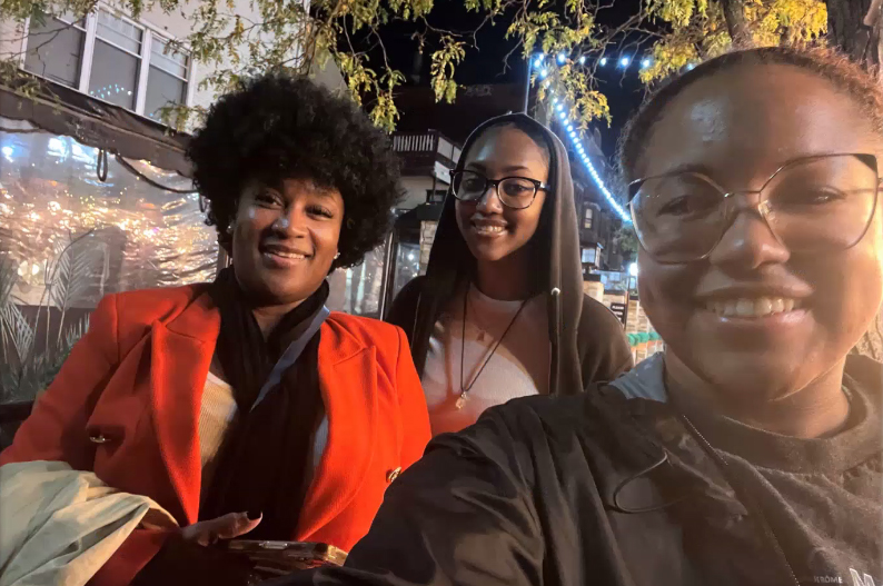 three woman smile for a selfie outside in the dusk