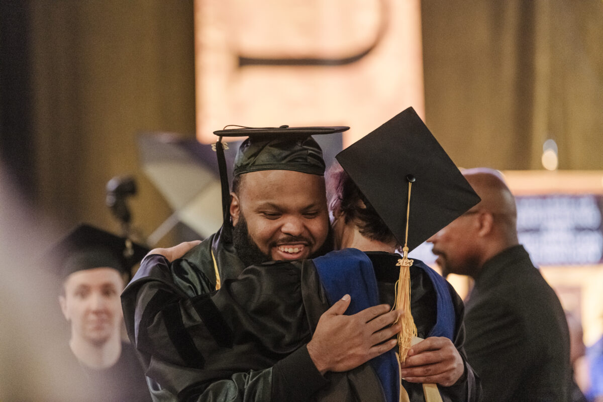 A graduate in robes hugs a professor