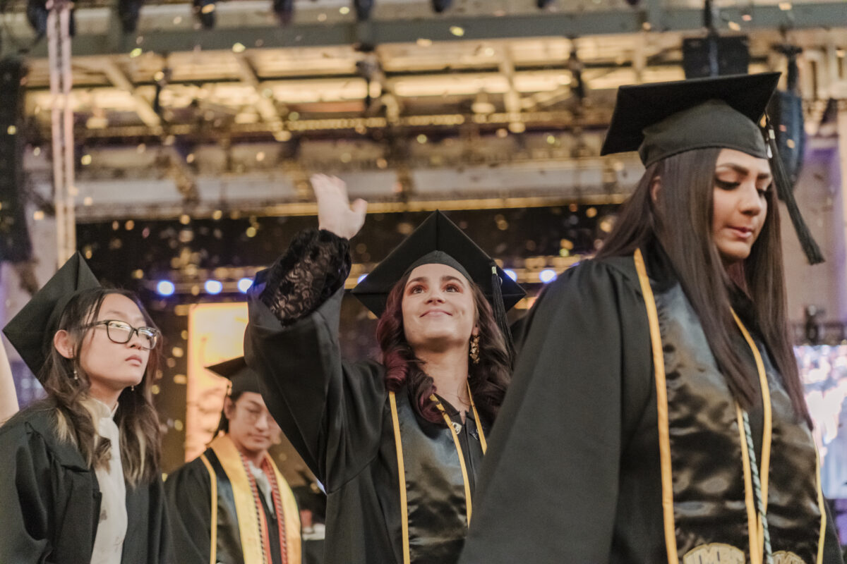 A graduate processes out waving while confetti falls 