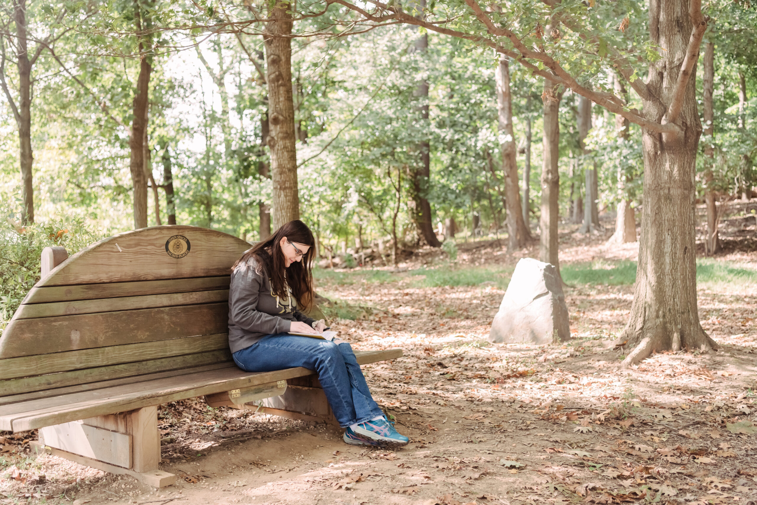 a woman writes in a journal on a bench in a park