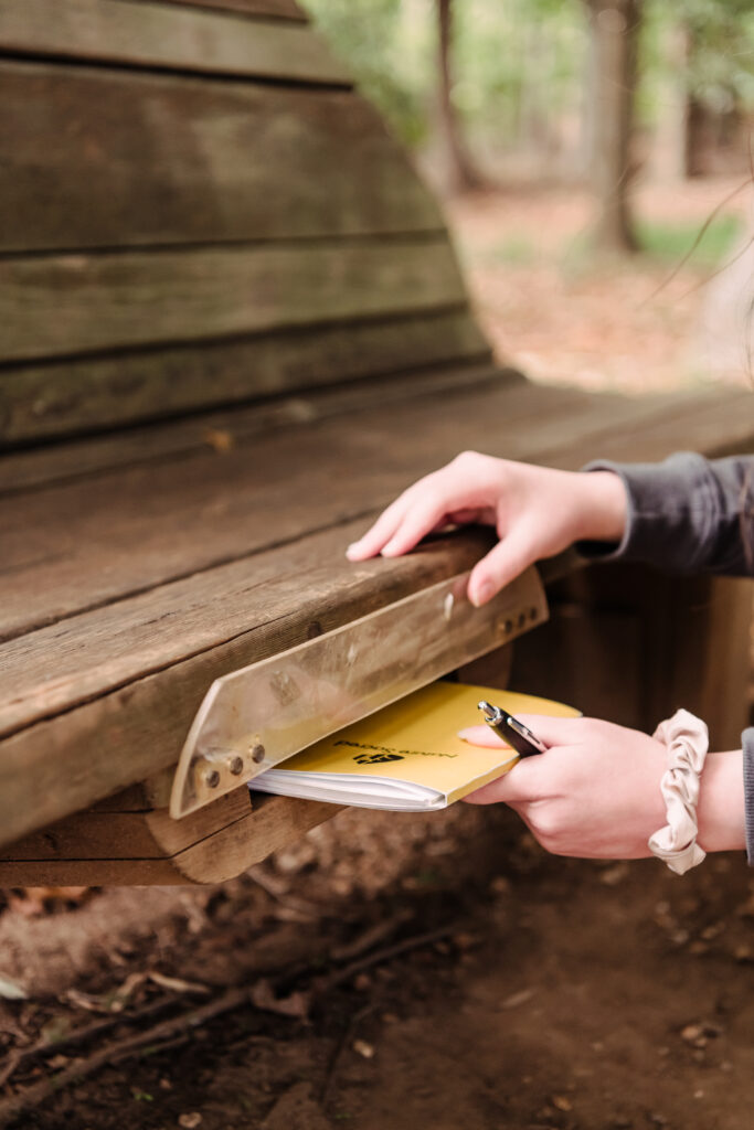 a hand returns one of the nature sacred journals to a special shelf under a bench in a park