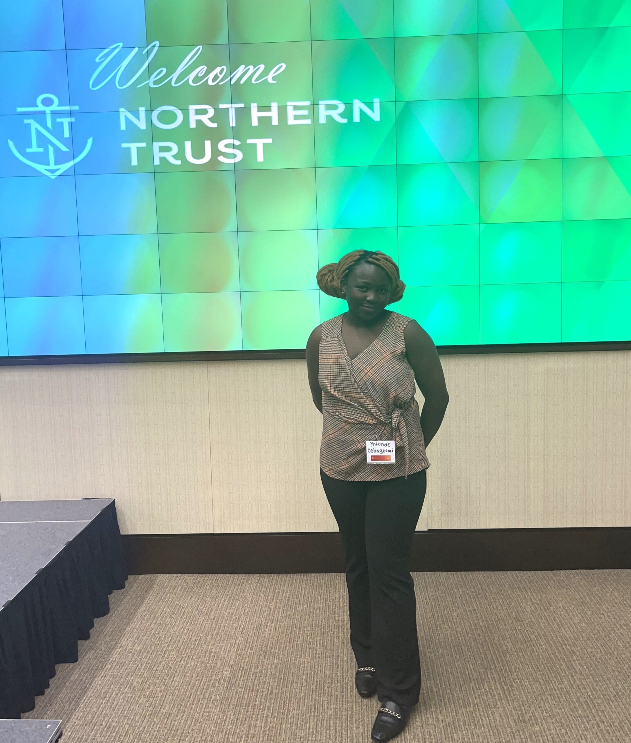 Yetunde Oshagbemi standing in front of a large screen that says welcome northern trust. 