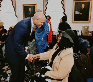 a man bends down to shake hands with a woman with disabilities using a wheelchair