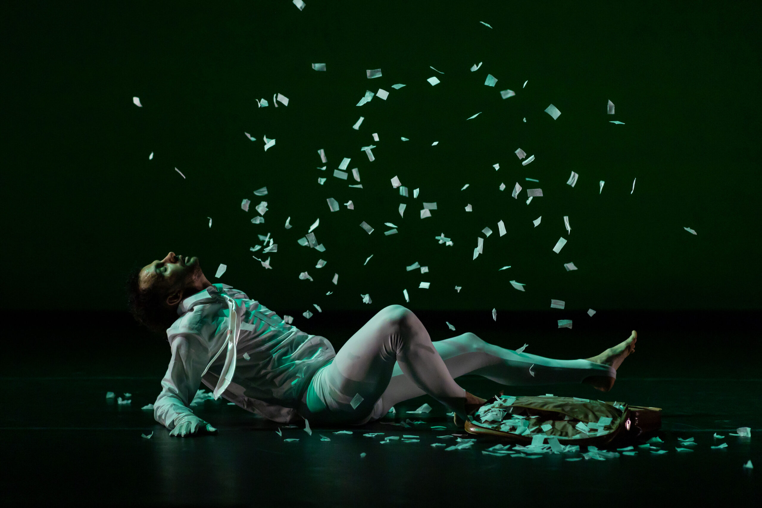 In a dark image, confetti rains down on a dancer who lies on the floor