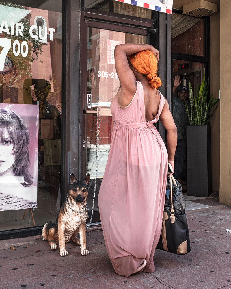 A Black woman in a pink dress looks into the window of a hair salon
